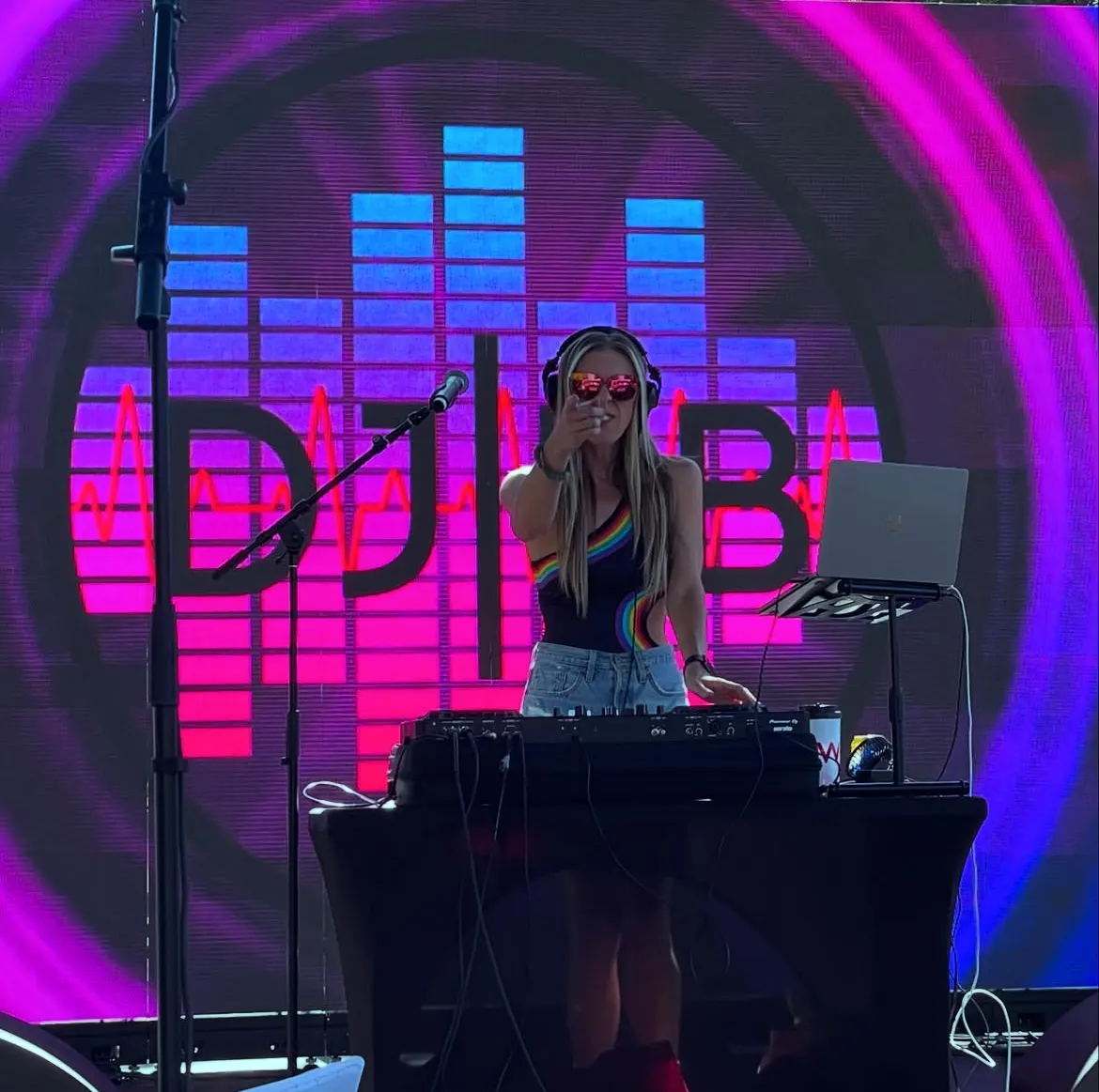DJ Lyndsay Brown in front of an LED wall showing her DJ LB logo